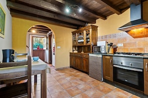 A kitchen with wooden cabinets, a microwave, an oven, and a dining area with a table and chairs. - Country House 'Esteiro' with Shared Garden and Wi-Fi (Espesante)