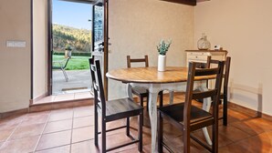 Un comedor con una mesa redonda, sillas de madera, un florero con flores y una botella sobre una mesita.