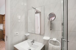 A bathroom with a white sink, a mirror, a glass shower enclosure, and a towel rack.