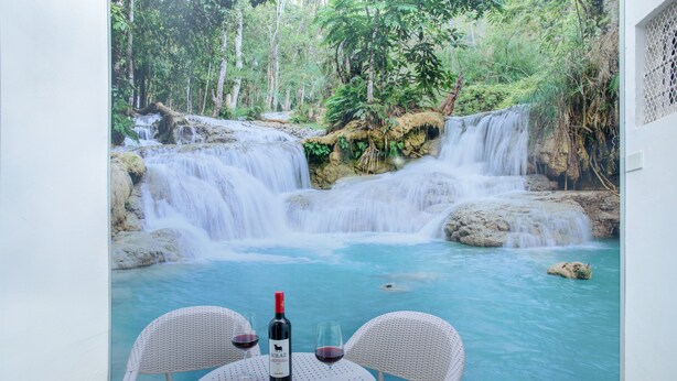 Una mesa con una botella de vino, dos copas y un plato de comida, con vista a una cascada y una piscina.