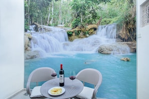 Une table avec une bouteille de vin, deux verres et une assiette de nourriture, donnant sur une cascade et une piscine.