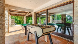 A foosball table in a covered outdoor area with stone walls and a view of greenery. - Holiday Home 'Du Parc' with Shared Pool, Lake View & Wi-Fi (Genouillé)