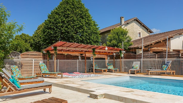 A swimming pool with lounge chairs and a pergola, surrounded by a stone house and greenery. - Holiday Home 'Du Parc' with Shared Pool, Lake View & Wi-Fi (Genouillé)