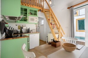 A kitchen with a wooden staircase, a white chair, a wooden bowl, and a white table.