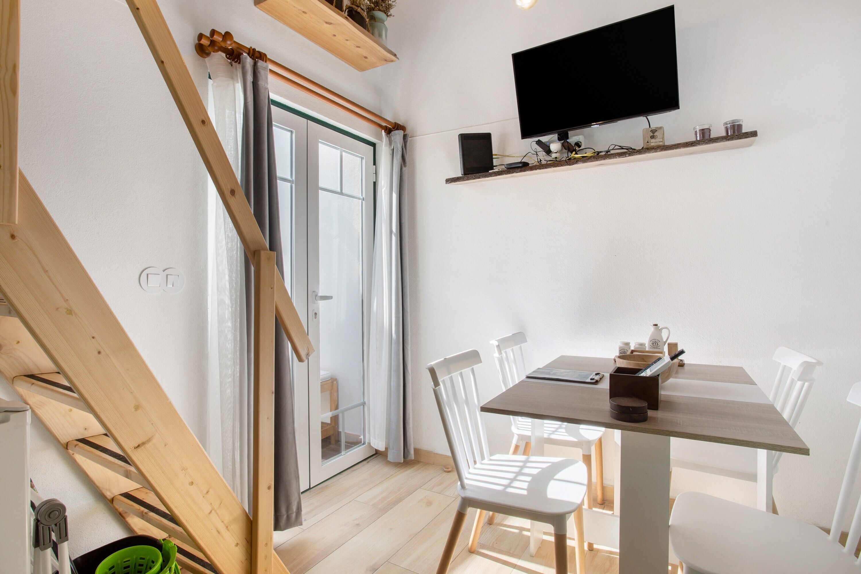 Un espace repas comprenant une table, des chaises, un téléviseur fixé au mur et une porte-fenêtre coulissante donnant sur un espace extérieur.