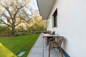 A patio with a table and chairs, a tree, and a well-maintained lawn.
