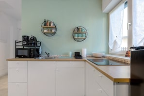 A kitchen with a microwave, coffee maker, and shelves with jars and cups.