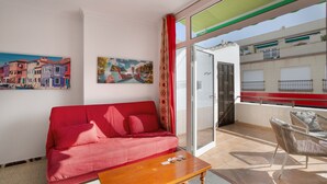 A red sofa, a wooden table, and a balcony with wicker chairs. - Vacation Apartment 'Los Angeles 1' with Sea View, Shared Terrace and Wi-Fi (Playa de Mogán)