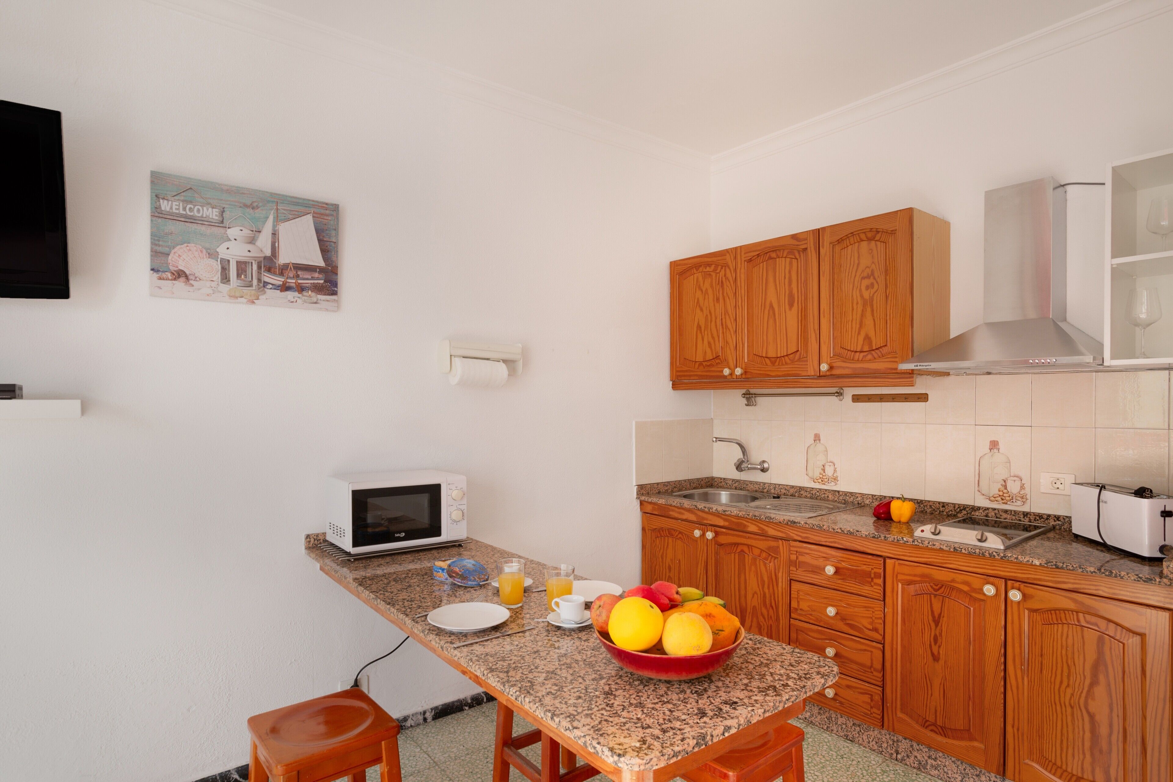 A kitchen with wooden cabinets, a microwave, a sink, and a fruit bowl on the counter.