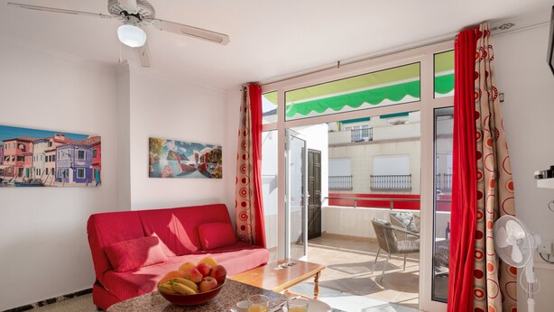 A room with a red sofa, a dining table with breakfast items, a fan, and a view of a balcony. - Vacation Apartment 'Los Angeles 1' with Sea View, Shared Terrace and Wi-Fi (Playa de Mogán)