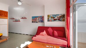A living room with a red sofa, a wooden coffee table, a ceiling fan, and two wall-mounted paintings. - Vacation Apartment 'Los Angeles 1' with Sea View, Shared Terrace and Wi-Fi (Playa de Mogán)