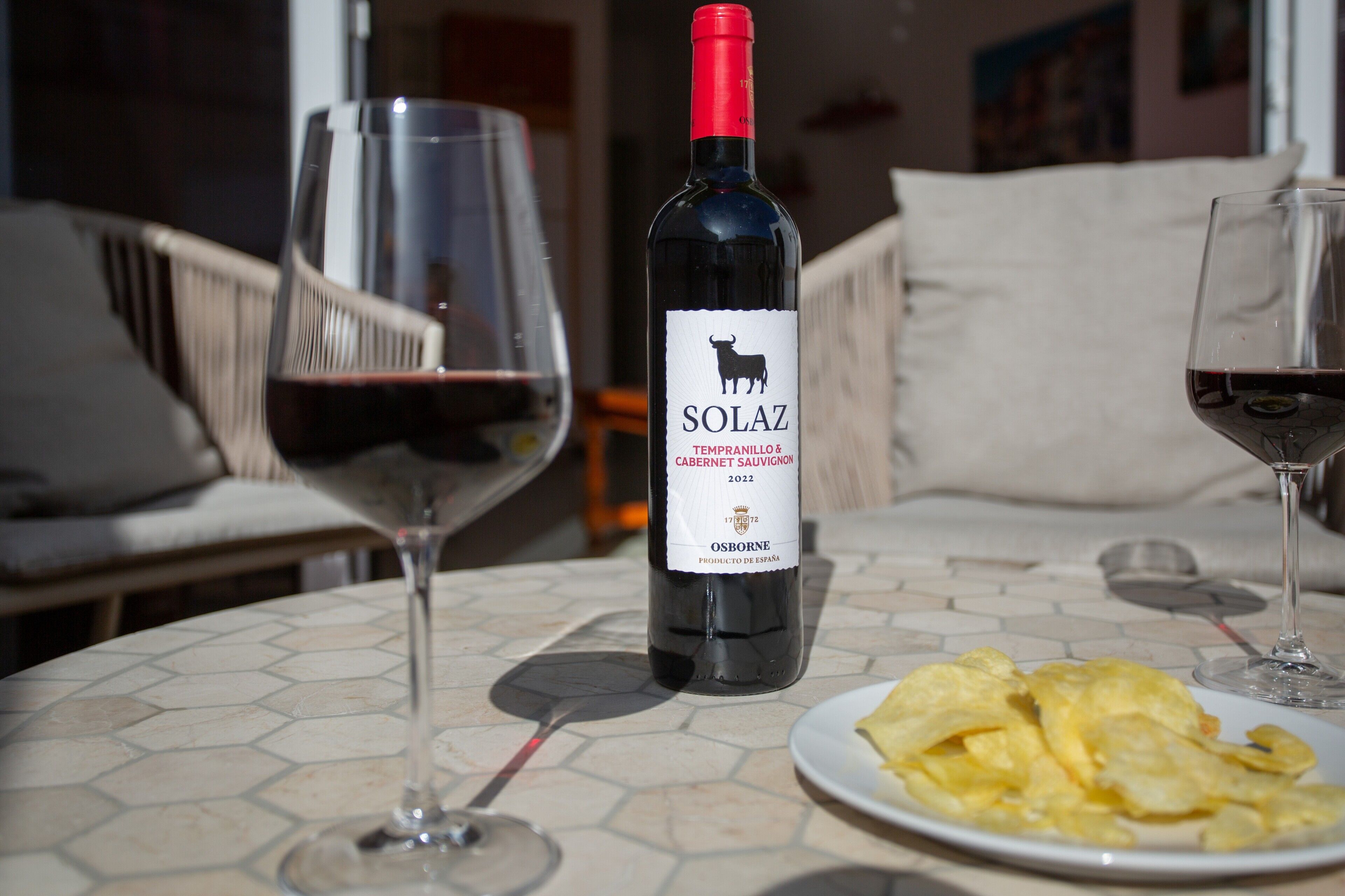 A table with a bottle of Solaz 2022 wine, two wine glasses, and a plate of chips.