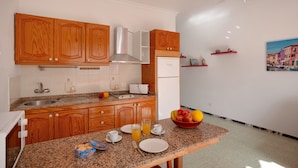 A kitchen with wooden cabinets, a stainless steel range hood, a refrigerator, and a breakfast setup with plates, cups, and a bowl of fruit. - Vacation Apartment 'Los Angeles 1' with Sea View, Shared Terrace and Wi-Fi (Playa de Mogán)