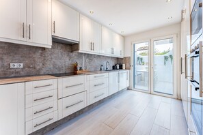 A modern kitchen with white cabinets, a concrete backsplash, and a sliding glass door leading to an outdoor area.