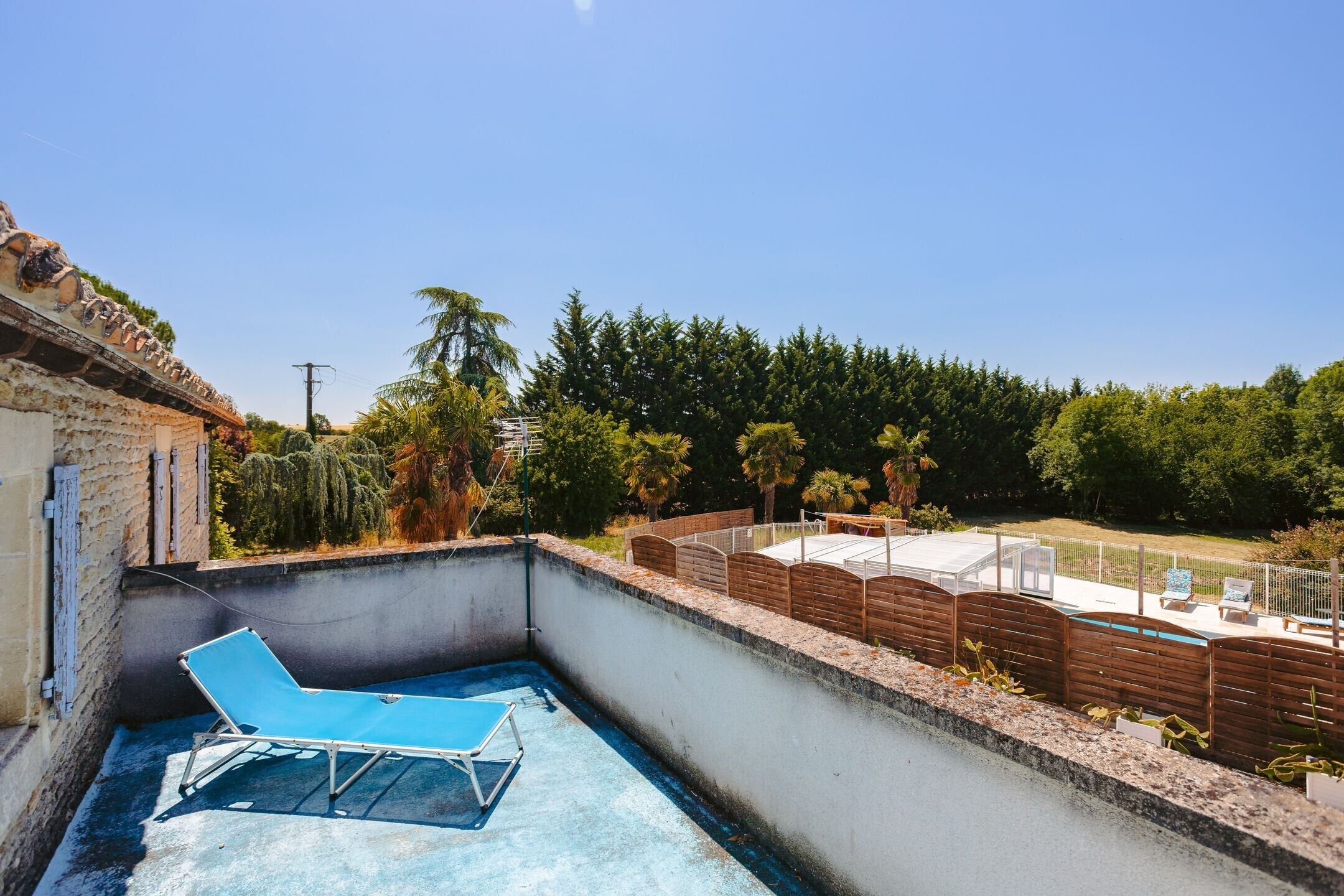A rooftop terrace with a pool, lounge chairs, and a view of a forested area.