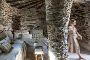 A stone-walled room with a sofa, a small table, and a vase with branches.