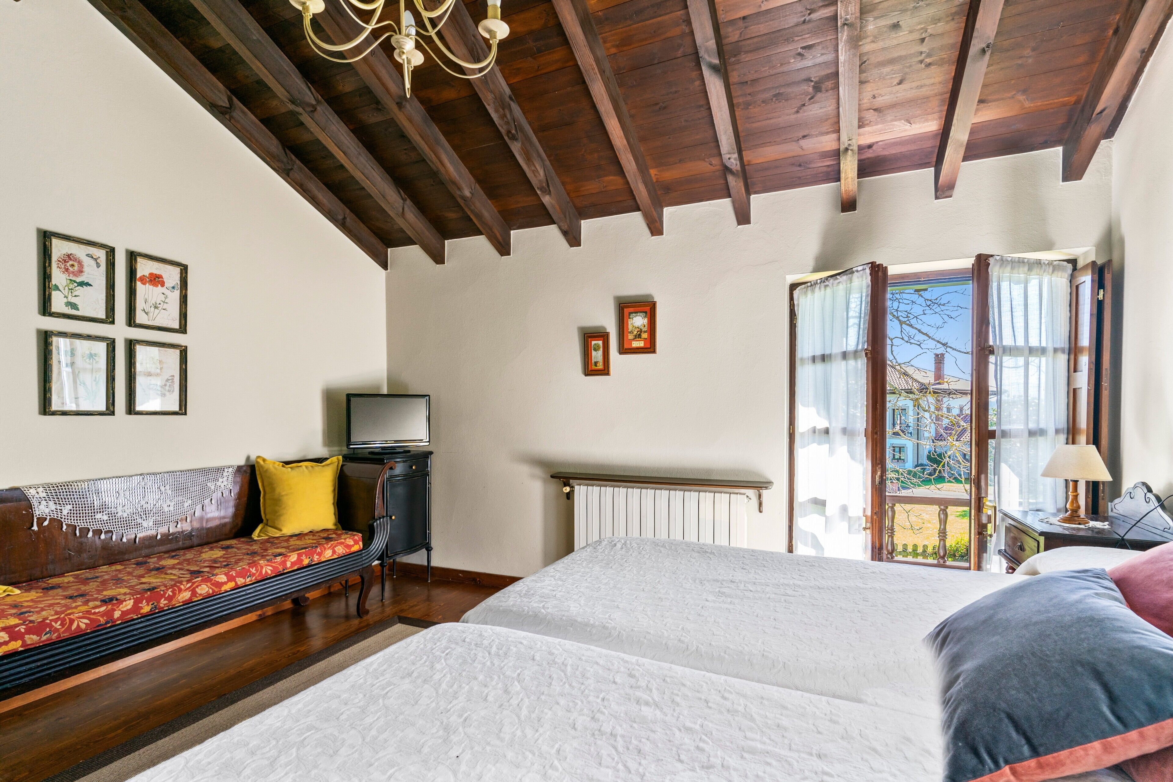 A bedroom with a wooden ceiling, a bed, a sofa, a radiator, and a window with curtains.