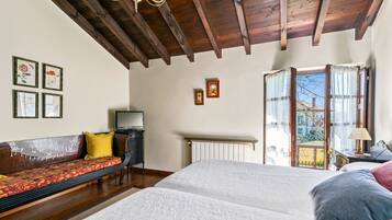 A bedroom with a wooden ceiling, a bed, a sofa, a radiator, and a window with curtains.