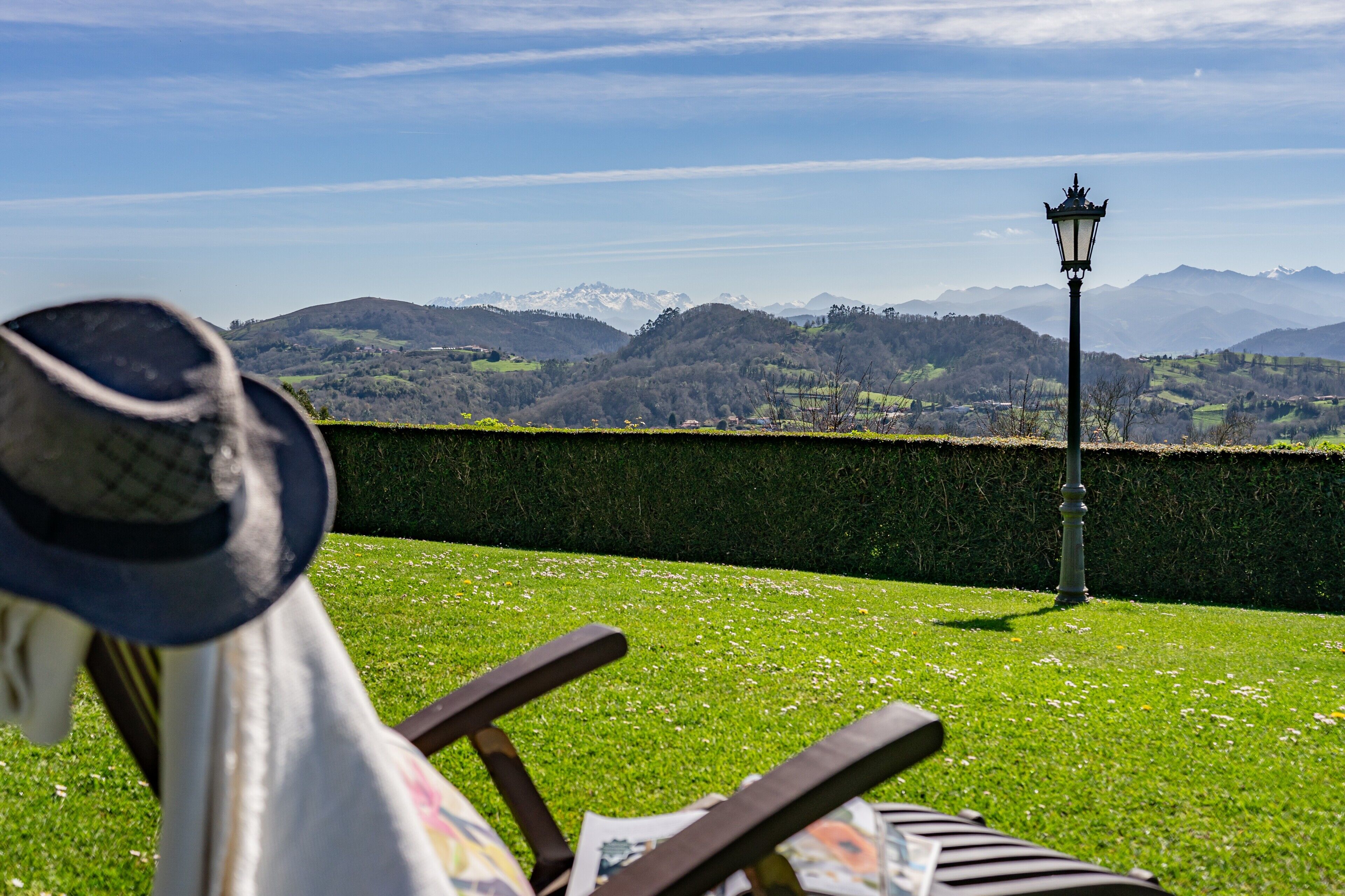 A view of a grassy area with a bench, a lamp post, and a mountain range in the background.