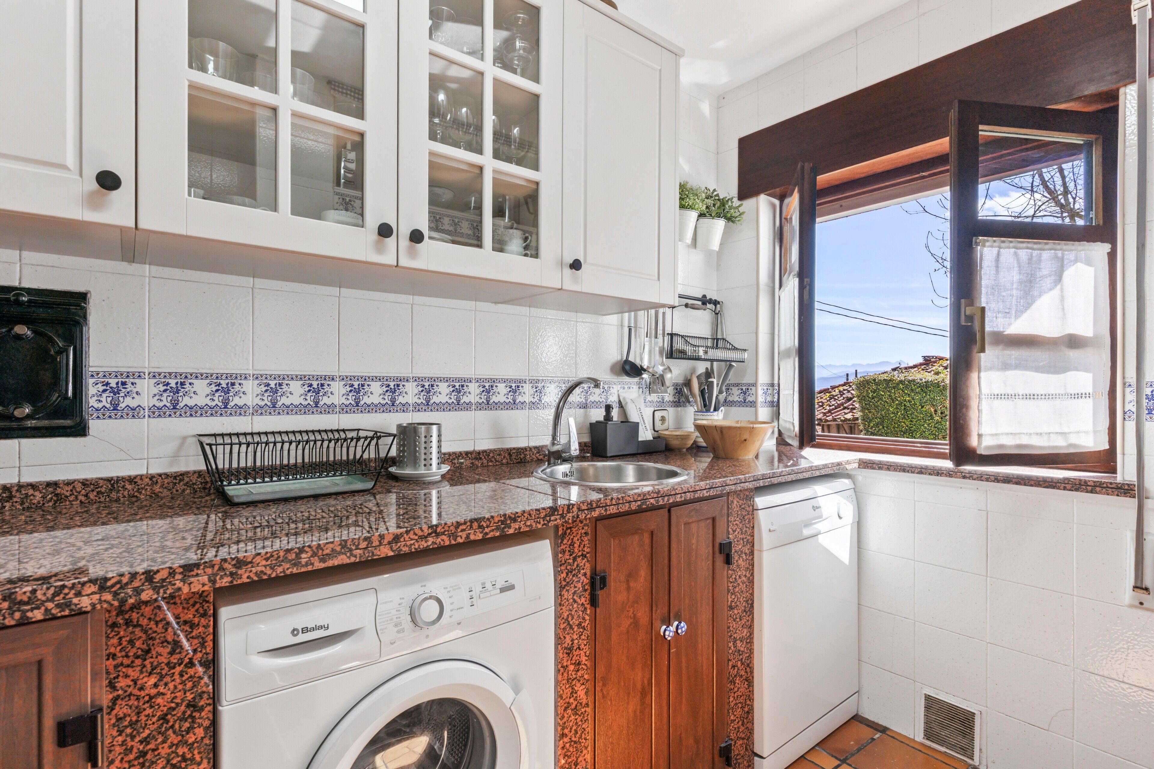 Una cocina con armarios blancos, lavadora y ventana con vistas.