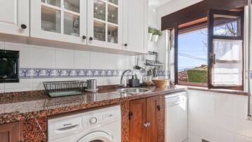 Una cocina con armarios blancos, lavadora y ventana con vistas.