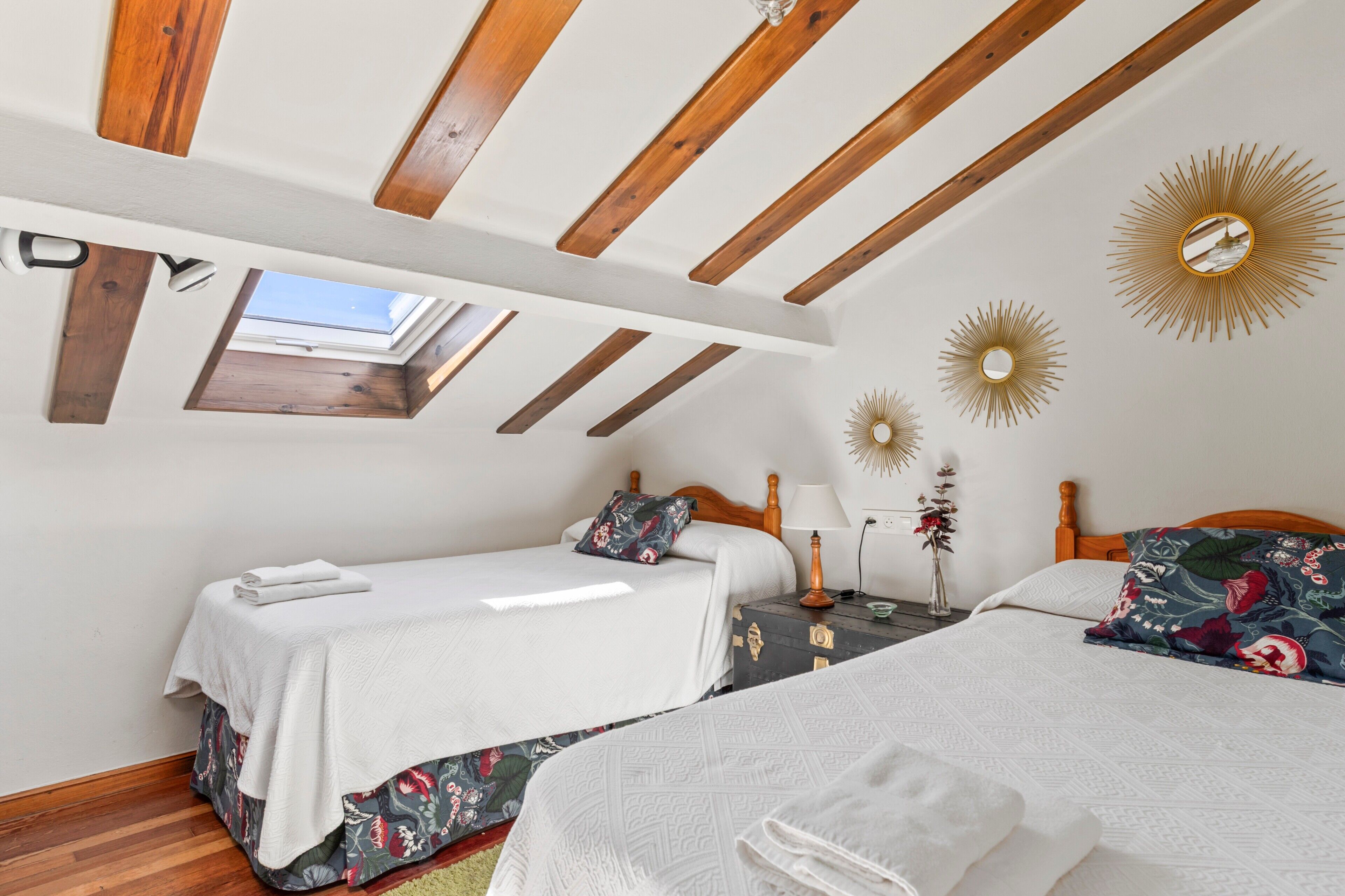 Dormitorio con dos camas, vigas de madera, tragaluces y espejos decorativos en la pared.