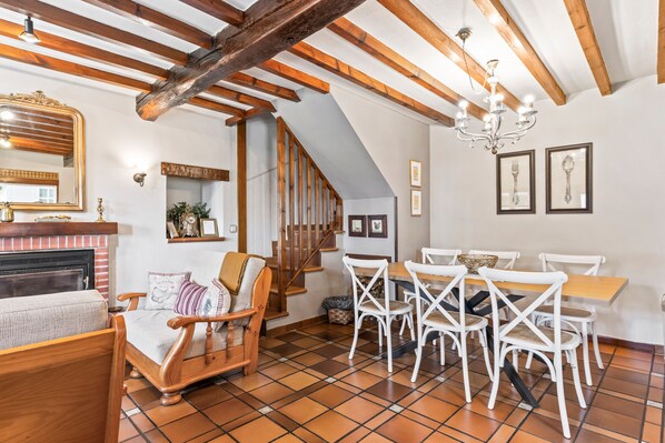 A dining area with a wooden table and white chairs, a fireplace, and a staircase.