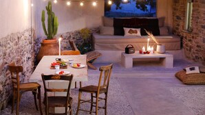 A cozy outdoor seating area with a stone wall, a cactus plant, string lights, a sofa, and a table with food and candles. - Apartment 'Onos Eco Living Tinos' with Mountain View, Wi-Fi and Air Conditioning (Falatados)