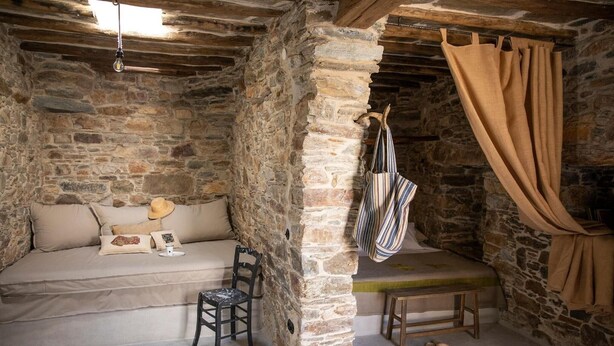 A rustic stone-walled room with a sofa, a hanging chair, and a bench. - Apartment 'Onos Eco Living Tinos' with Mountain View, Wi-Fi and Air Conditioning (Falatados)
