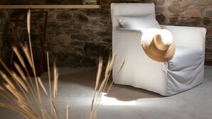 A stone wall, a white sofa, and a woven basket with sticks. - Apartment 'Onos Eco Living Tinos' with Mountain View, Wi-Fi and Air Conditioning (Falatados)