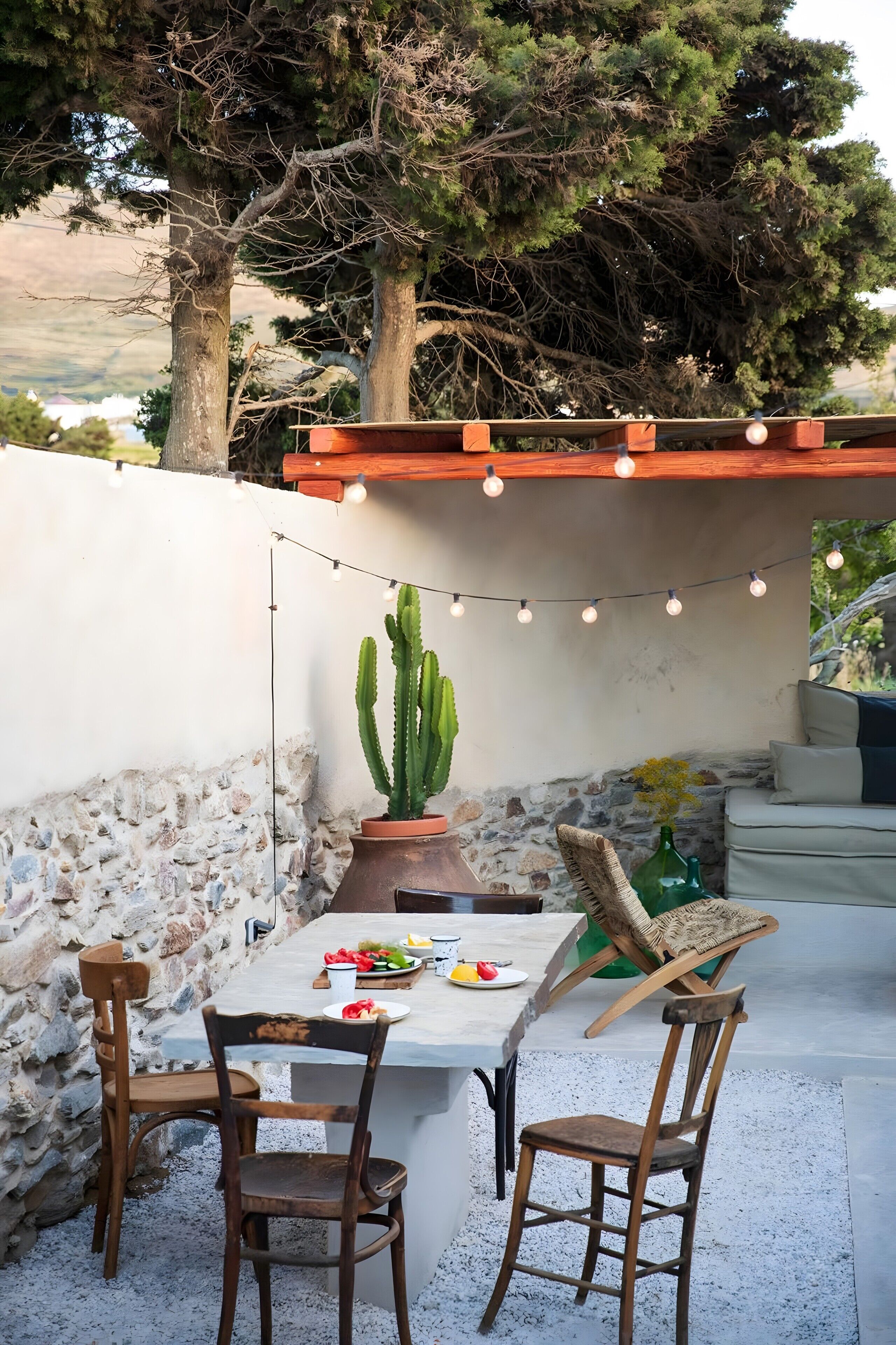 Een terras buiten met een tafel, stoelen, een cactus en lichtslingers.
