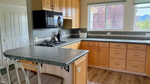 A kitchen with wooden cabinets, a black microwave, a gas stove, and a window with a view of trees. - Idyllic Vineyard Loft Apartment (Solvang)