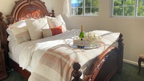 A neatly made bed with a decorative headboard, a bedside table, and a window with a view of trees. - Idyllic Vineyard Loft Apartment (Solvang)