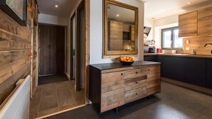 Een moderne keuken met een grote spiegel, houten keukenkastjes en een fruitschaal op het aanrecht.