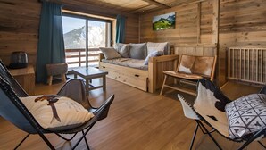 Een houten interieur met een bank, stoelen, een tafel en een raam met uitzicht op bergen.