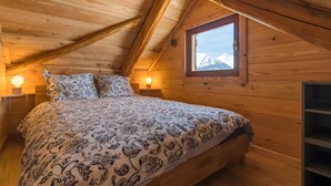 Een houten slaapkamer met een bed, twee bedlampjes, een raam met uitzicht en een inbouwkast.