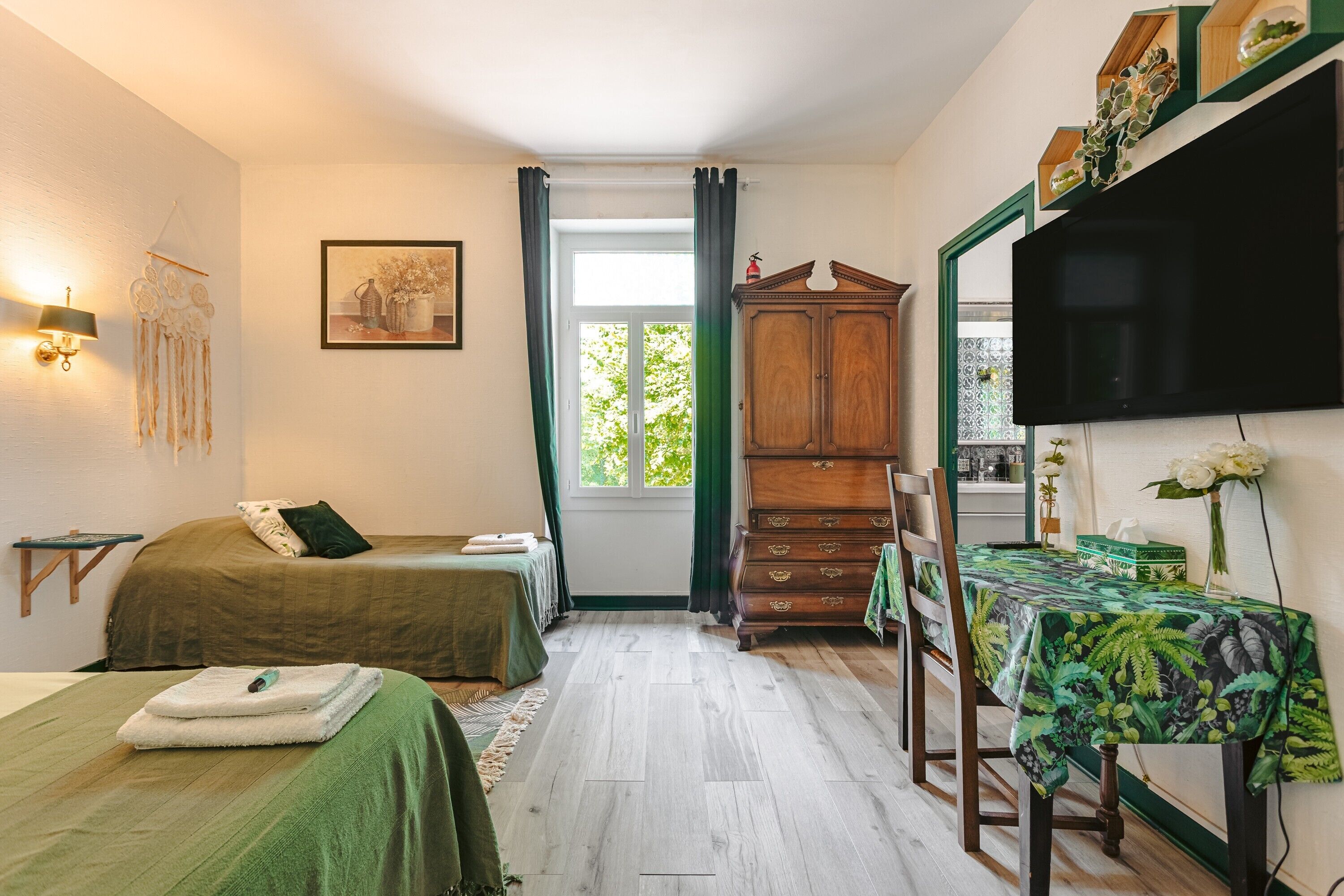Ein Zimmer mit einem Bett, einem Schreibtisch, einem Schrank, einem Fernseher und einem fenster mit Vorhängen.