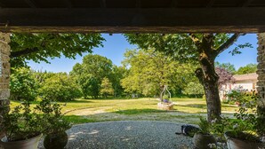 A covered patio with a gravel path, potted plants, and a view of a grassy yard with trees and a swing set.