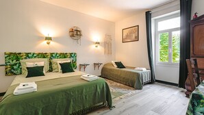 A room with two beds, a window with curtains, a wall-mounted light fixture, and a framed picture.