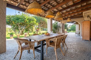 An outdoor dining area with wicker furniture, hanging woven light fixtures, and a view of greenery. - Finca 'Cas Forner' with Mountain Views, Private Pool and Wi-Fi (Illes Balears)