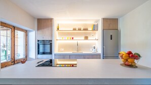 A modern kitchen with wooden cabinetry, a built-in oven, a refrigerator, and a fruit bowl on the counter. - Finca 'Cas Forner' with Mountain Views, Private Pool and Wi-Fi (Illes Balears)