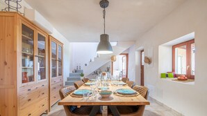 A dining area with a wooden table set for six, surrounded by wicker chairs, with a cabinet and staircase in the background. - Finca 'Cas Forner' with Mountain Views, Private Pool and Wi-Fi (Illes Balears)