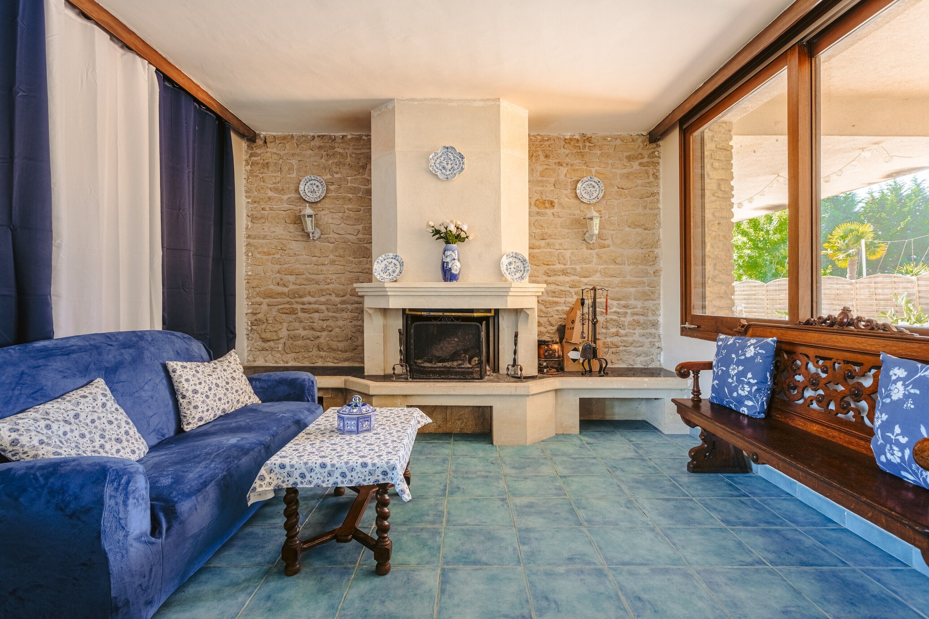 A living room with a fireplace, a blue sofa, a wooden bench, and a table with a blue tablecloth.