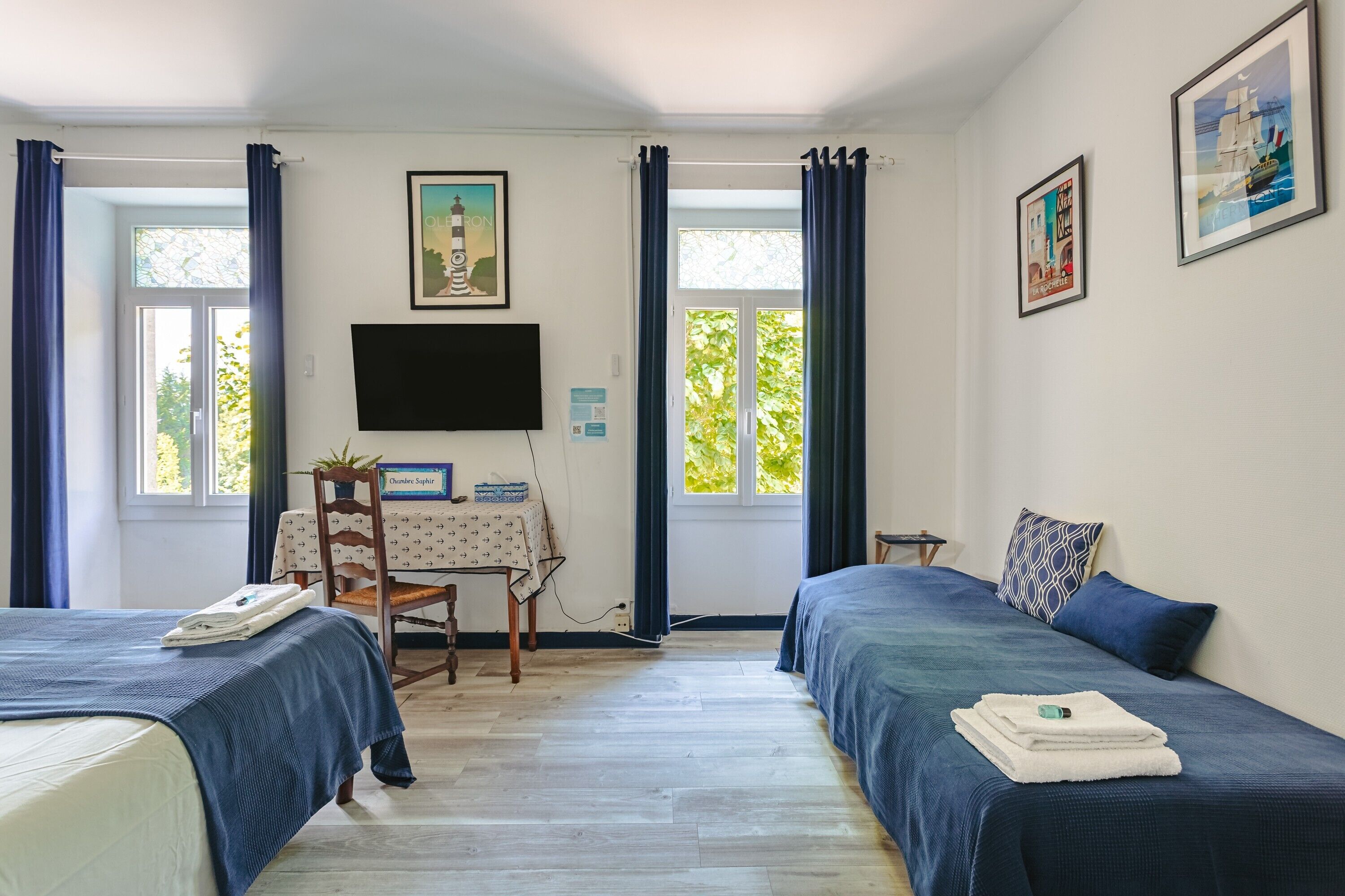 Habitación con dos camas, un escritorio, una silla, un televisor y cortinas.