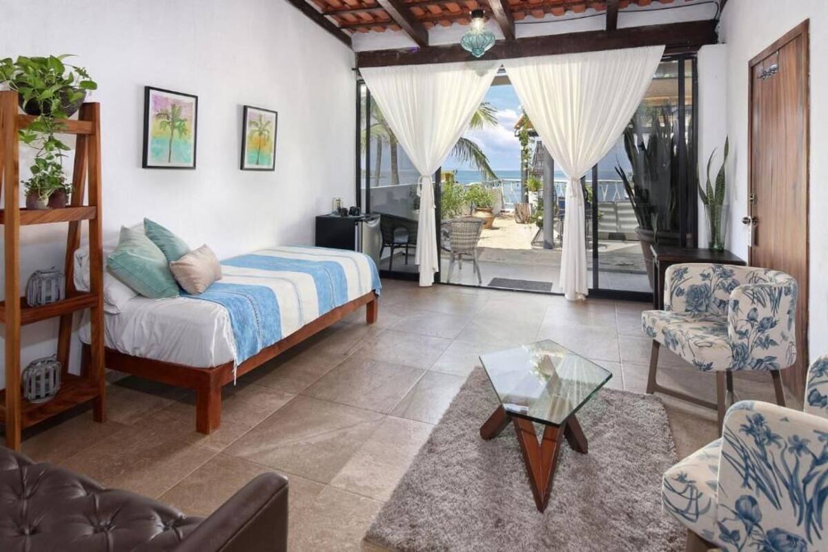 A bedroom with a bed, a desk, a chair, and a view of the beach.