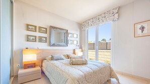 Ein Schlafzimmer mit einem Bett, Nachttischlampen, einem Nachttisch, einem großen Spiegel und gerahmten Bildern an der Wand.
