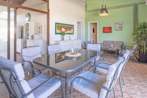 A dining area with a glass table and metal chairs, a sofa, a clock, and artwork on the walls.
