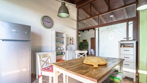A kitchen with a wooden table, a refrigerator, and a clock on the wall. - Villa 'Apollonion' with Private Pool, Wi-Fi and Air Conditioning (Siracusa)