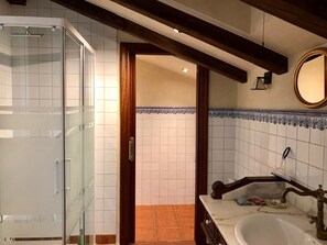 Une salle de bain dotée d’une douche à parois de verre, d’un lavabo avec un plan de toilette en marbre et d’un sol carrelé.