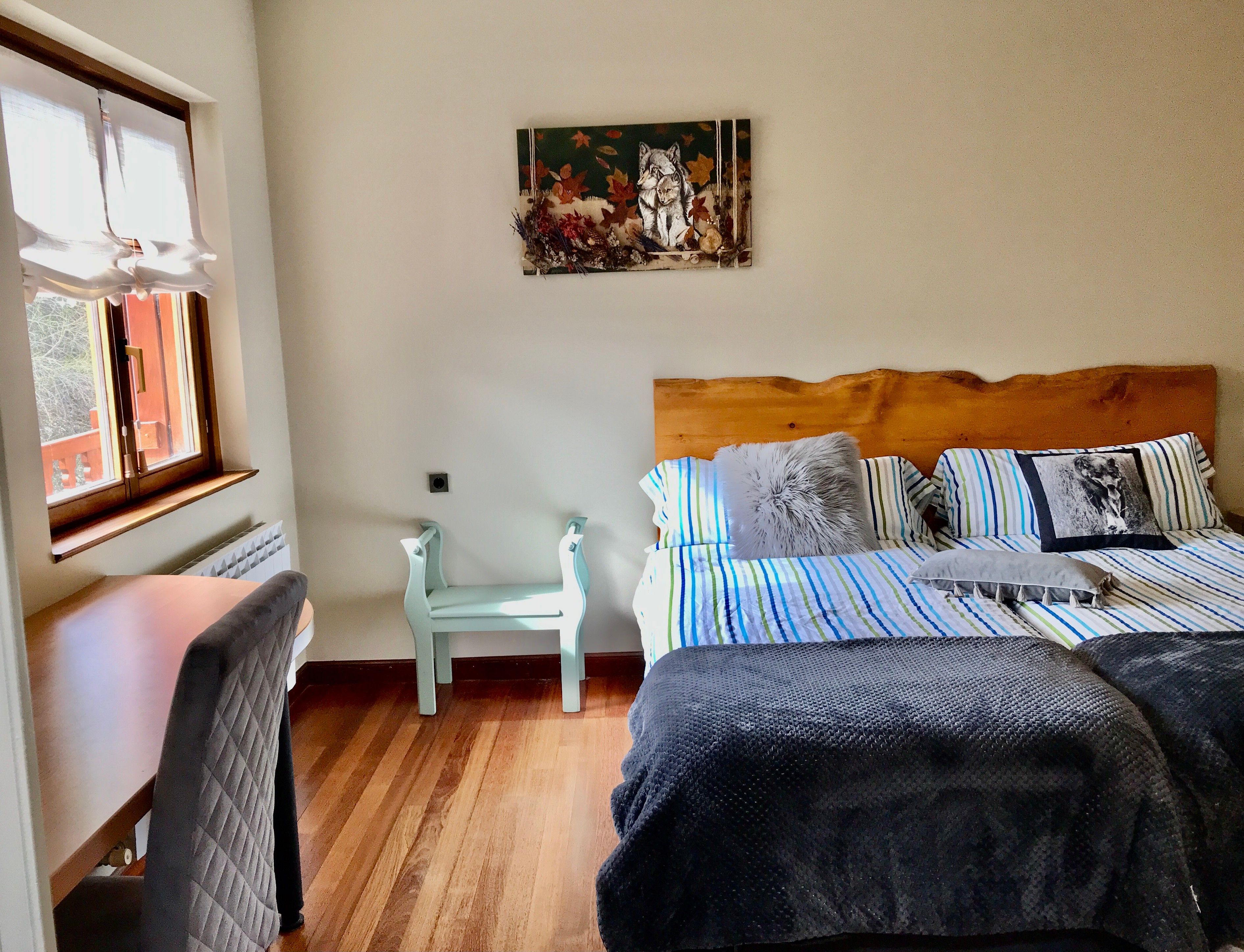 A bedroom with a wooden headboard, a bed with striped bedding, a chair, and a painting on the wall.
